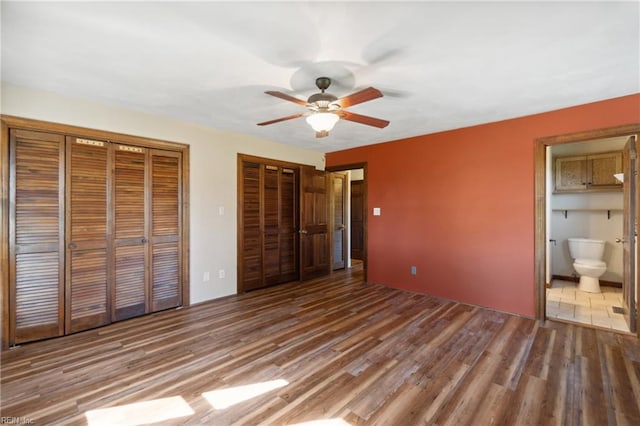 unfurnished bedroom featuring multiple closets, wood-type flooring, connected bathroom, and ceiling fan