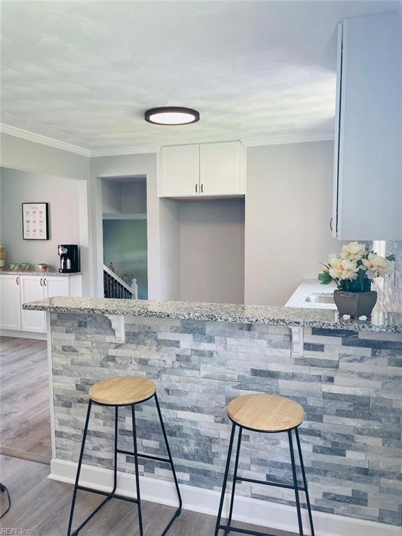 bar featuring light wood-type flooring, light stone countertops, crown molding, and white cabinetry