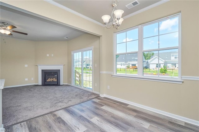 unfurnished living room with ornamental molding, carpet, a wealth of natural light, and ceiling fan with notable chandelier