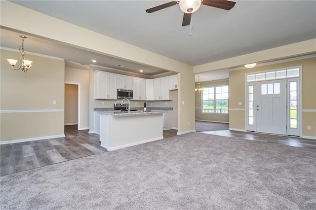 kitchen featuring hanging light fixtures, white cabinets, light stone counters, ceiling fan with notable chandelier, and dark colored carpet