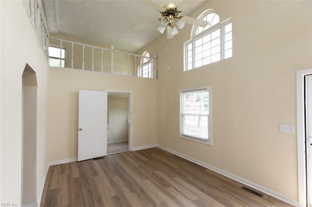 empty room featuring ceiling fan, hardwood / wood-style flooring, and a high ceiling