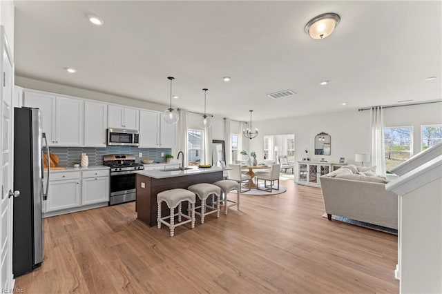 kitchen featuring hanging light fixtures, a kitchen breakfast bar, stainless steel appliances, an island with sink, and white cabinets