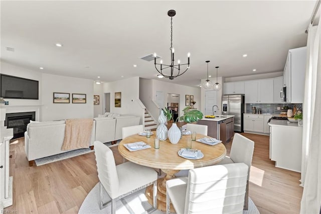 dining area with an inviting chandelier, sink, and light hardwood / wood-style flooring