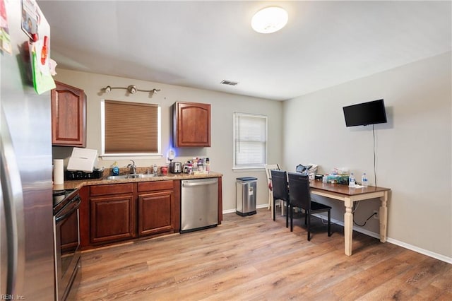 kitchen featuring light wood-type flooring, stainless steel appliances, light stone counters, and sink