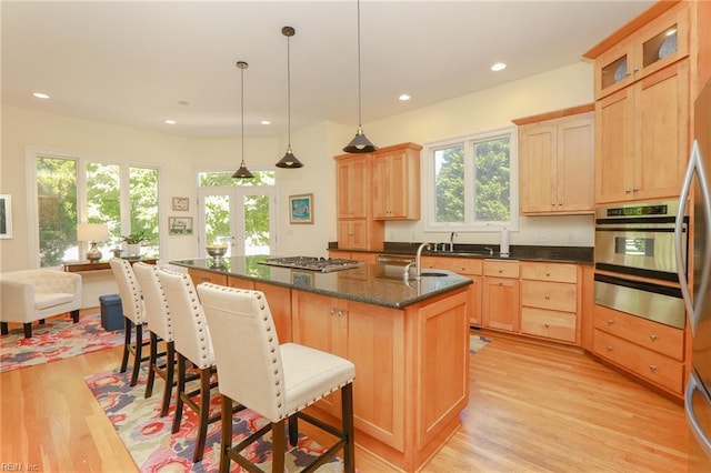 kitchen featuring appliances with stainless steel finishes, a kitchen island with sink, hanging light fixtures, a kitchen breakfast bar, and light wood-type flooring