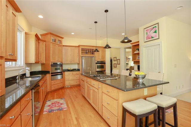 kitchen with sink, a kitchen island with sink, stainless steel appliances, decorative light fixtures, and light wood-type flooring