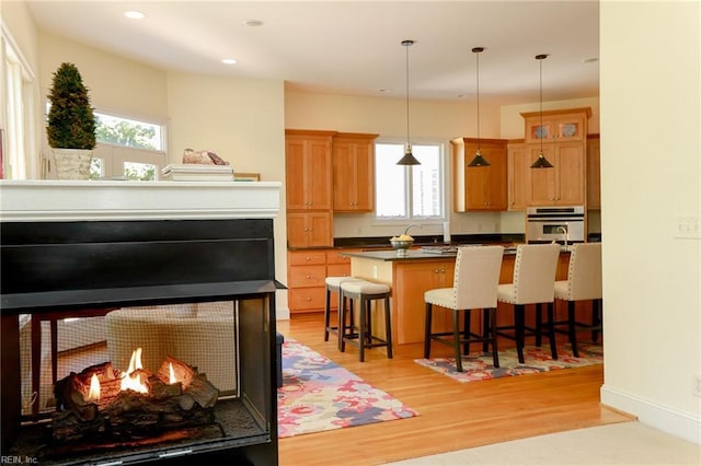 kitchen featuring a breakfast bar, a kitchen island with sink, light hardwood / wood-style floors, decorative light fixtures, and oven