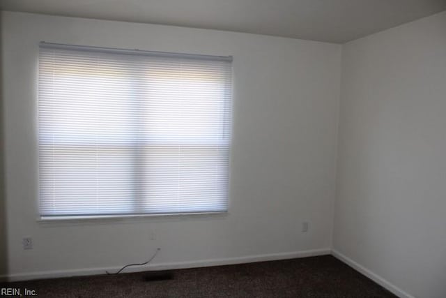 empty room featuring plenty of natural light and dark colored carpet