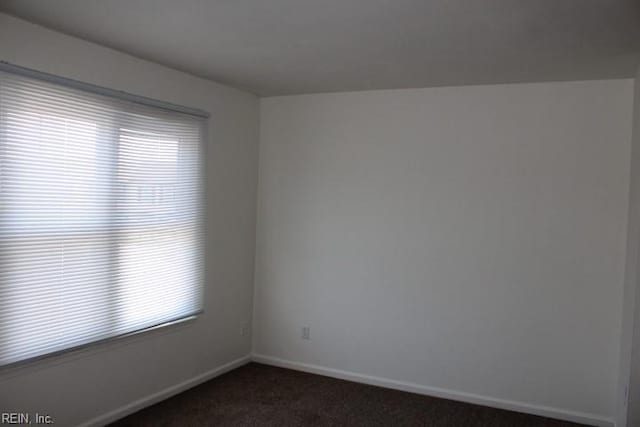 spare room with dark colored carpet and a wealth of natural light