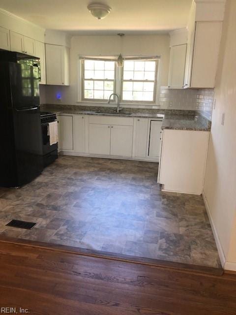 kitchen featuring range, white cabinets, dark wood-type flooring, black fridge, and decorative backsplash