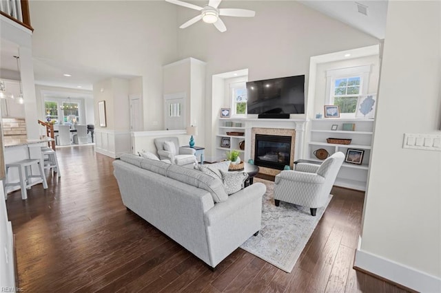 living room featuring a towering ceiling, built in shelves, dark hardwood / wood-style flooring, and ceiling fan