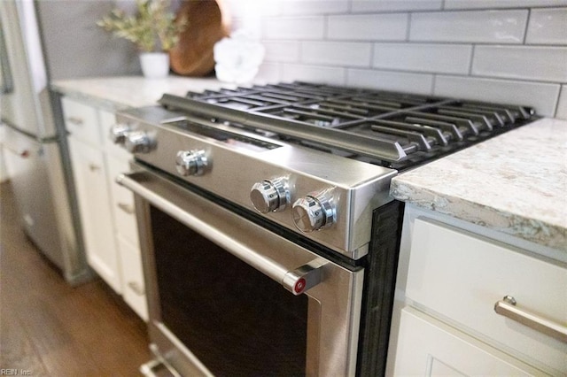 interior details featuring decorative backsplash, white cabinets, hardwood / wood-style floors, light stone counters, and stainless steel range