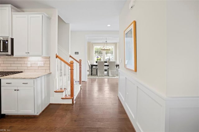 hall with recessed lighting, a decorative wall, dark wood-style flooring, stairs, and wainscoting
