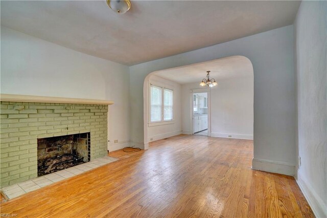 unfurnished living room with an inviting chandelier, a fireplace, and light wood-type flooring