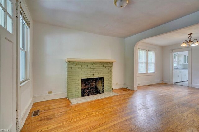 unfurnished living room featuring hardwood / wood-style flooring, a chandelier, and a brick fireplace