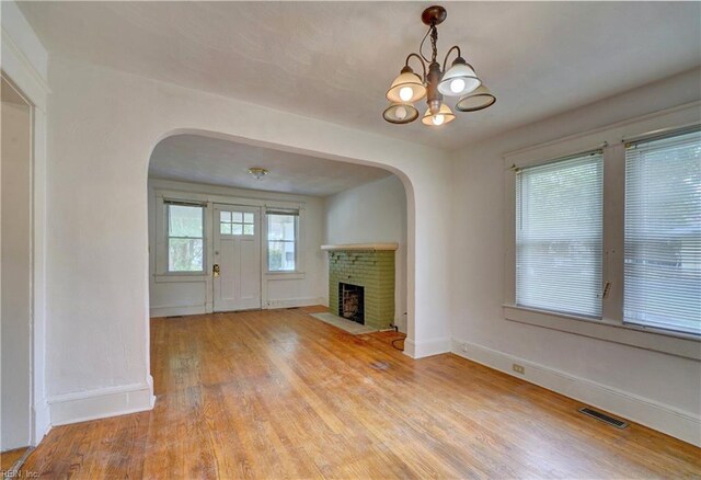 unfurnished living room featuring an inviting chandelier, a fireplace, and light hardwood / wood-style flooring