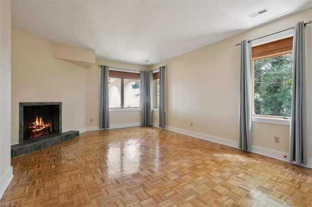 unfurnished living room with a tiled fireplace and light parquet flooring