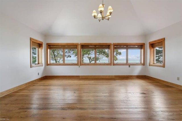 unfurnished room featuring lofted ceiling, wood-type flooring, and an inviting chandelier