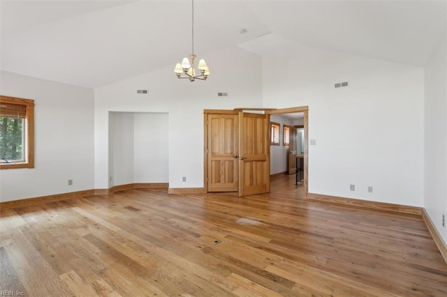 empty room featuring a notable chandelier, high vaulted ceiling, and light wood-type flooring