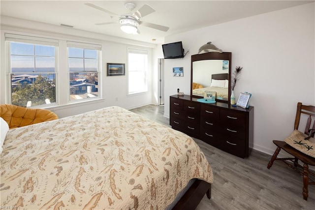 bedroom with ceiling fan, wood finished floors, visible vents, and baseboards