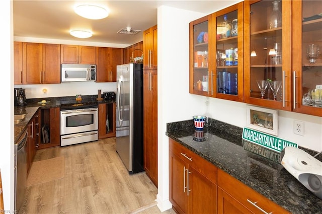 kitchen with light wood-style flooring, visible vents, appliances with stainless steel finishes, dark stone countertops, and glass insert cabinets