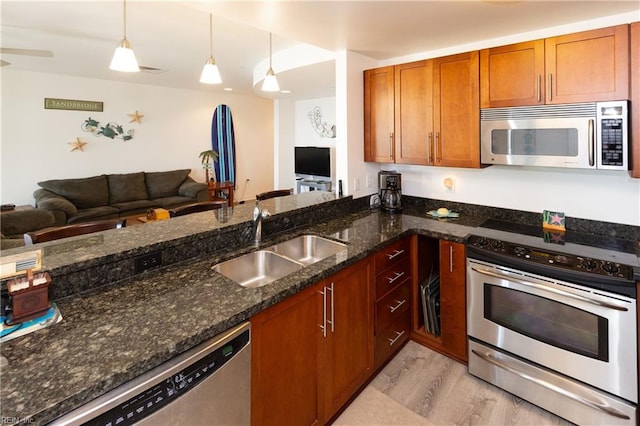 kitchen featuring decorative light fixtures, stainless steel appliances, open floor plan, a sink, and dark stone counters