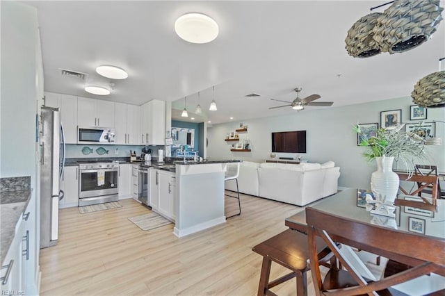 kitchen featuring visible vents, appliances with stainless steel finishes, open floor plan, white cabinetry, and a peninsula