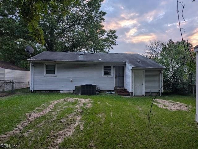 back house at dusk featuring central AC unit and a yard