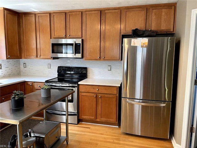 kitchen with appliances with stainless steel finishes, light wood-type flooring, and backsplash