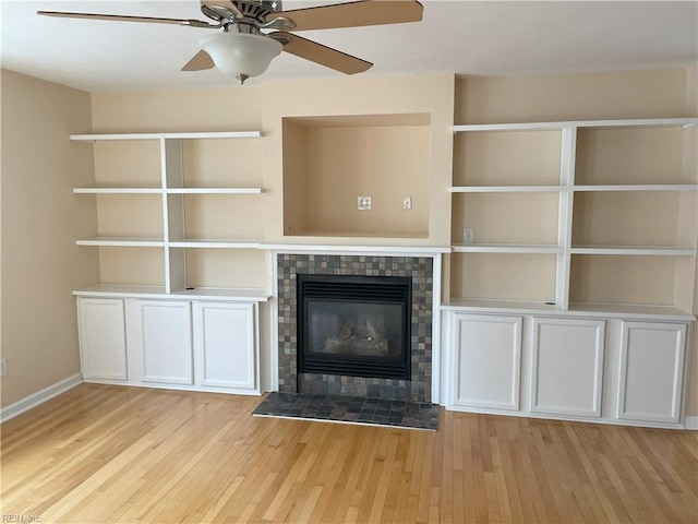 unfurnished living room featuring a fireplace, light wood-type flooring, ceiling fan, and built in shelves