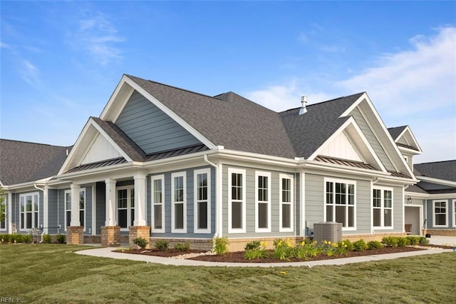 back of house with a shingled roof, a standing seam roof, and a lawn