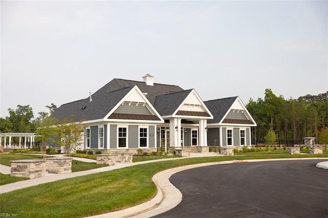 view of front of property with metal roof, roof with shingles, a standing seam roof, a front lawn, and a pergola