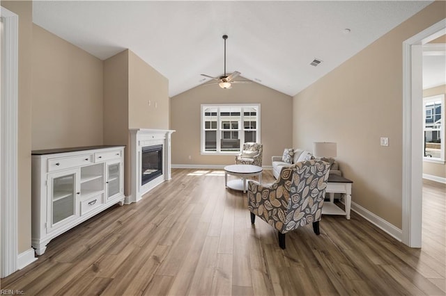 living area featuring ceiling fan, wood finished floors, baseboards, vaulted ceiling, and a glass covered fireplace