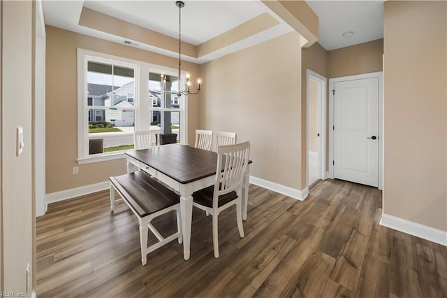 dining room featuring an inviting chandelier, baseboards, a raised ceiling, and wood finished floors