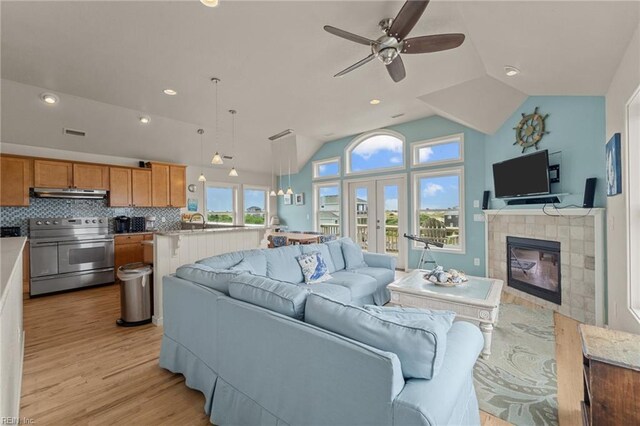 living room featuring a tiled fireplace, light hardwood / wood-style flooring, lofted ceiling, and ceiling fan