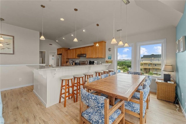 dining space with light wood-style flooring, visible vents, vaulted ceiling, and baseboards