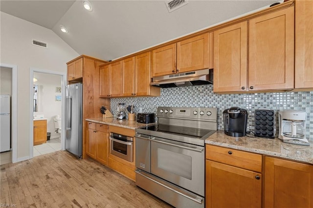 kitchen featuring light hardwood / wood-style flooring, light stone countertops, vaulted ceiling, backsplash, and stainless steel appliances