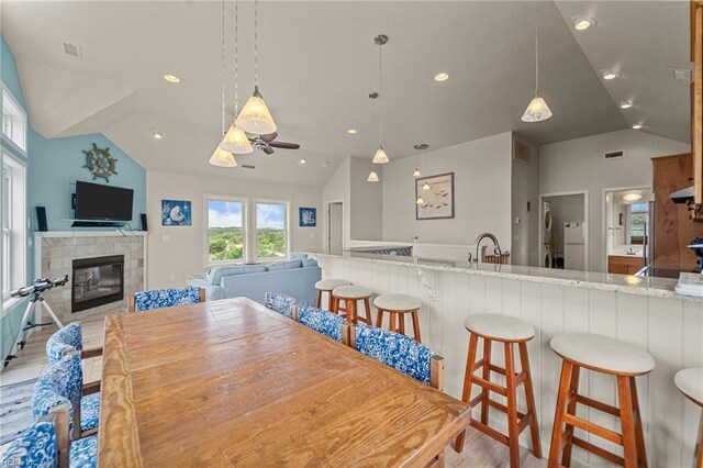 dining space featuring light hardwood / wood-style flooring, a fireplace, sink, and vaulted ceiling