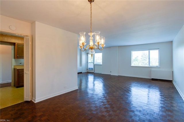 spare room with a chandelier, a healthy amount of sunlight, and dark parquet flooring