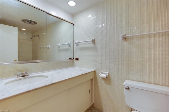 bathroom with backsplash, vanity, a tile shower, tile walls, and toilet