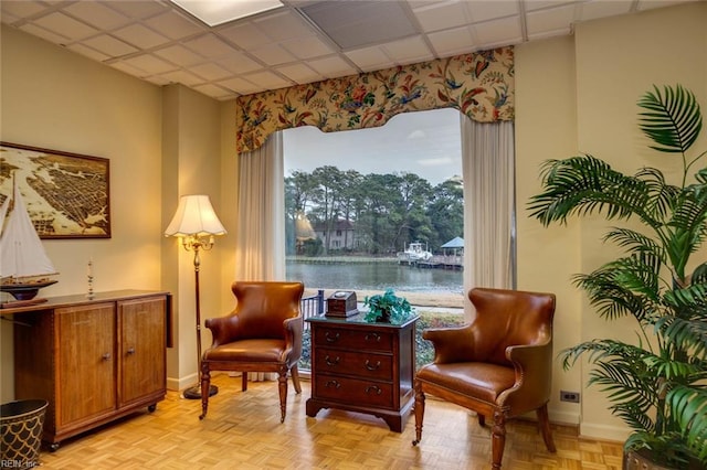 living area with light parquet flooring, a paneled ceiling, and a water view