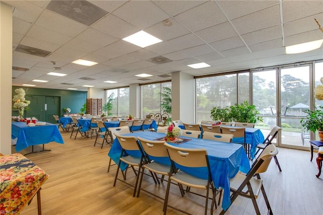 dining area with light wood-type flooring, a paneled ceiling, and floor to ceiling windows