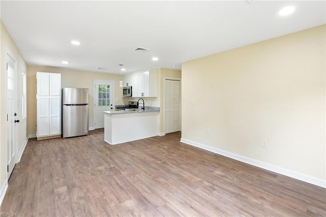 kitchen with white cabinetry, stainless steel appliances, light hardwood / wood-style flooring, and kitchen peninsula