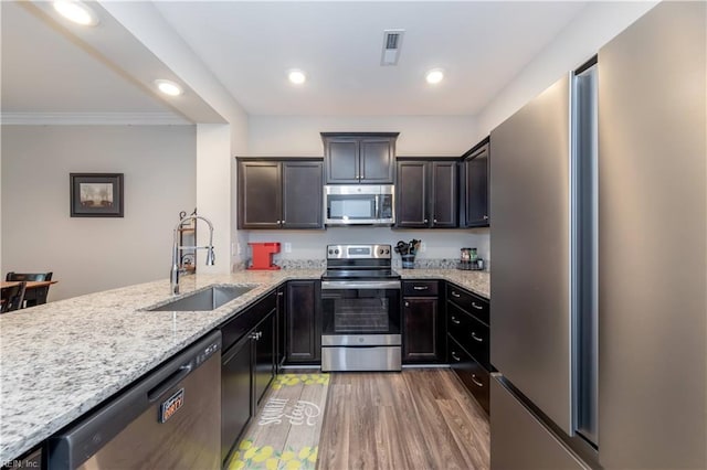 kitchen with dark brown cabinetry, sink, hardwood / wood-style flooring, stainless steel appliances, and light stone countertops