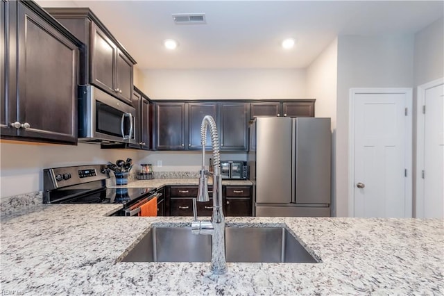 kitchen with dark brown cabinets, light stone countertops, stainless steel appliances, and sink