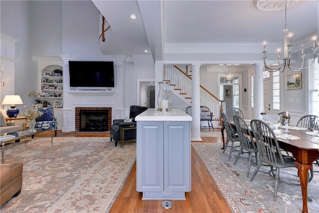 interior space with an inviting chandelier, ornamental molding, a brick fireplace, light wood-type flooring, and decorative columns