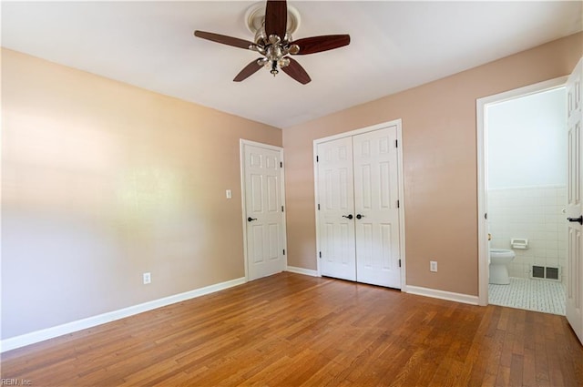 unfurnished bedroom featuring ceiling fan, ensuite bathroom, tile patterned flooring, and tile walls