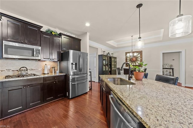 kitchen with dark wood-type flooring, pendant lighting, appliances with stainless steel finishes, light stone countertops, and a raised ceiling