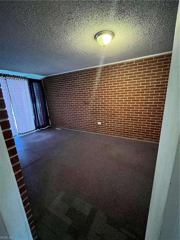 carpeted spare room featuring a textured ceiling and brick wall