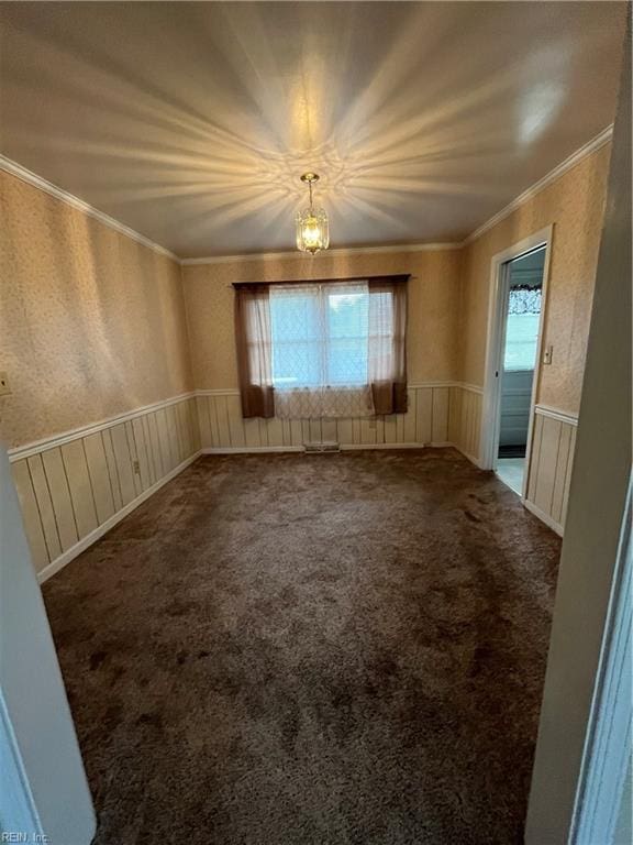 carpeted empty room with a healthy amount of sunlight, ornamental molding, and a chandelier